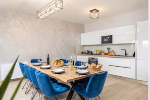 A modern kitchen with white cabinets, a microwave, and a dining area with blue chairs and a wooden table set for a meal. - Family Resort Santa Maria II Penthouse (Novalja)