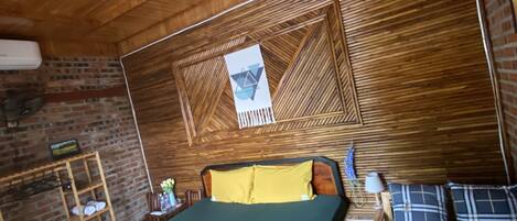 A room with a bed, a small table, a chair, and a wooden ceiling.