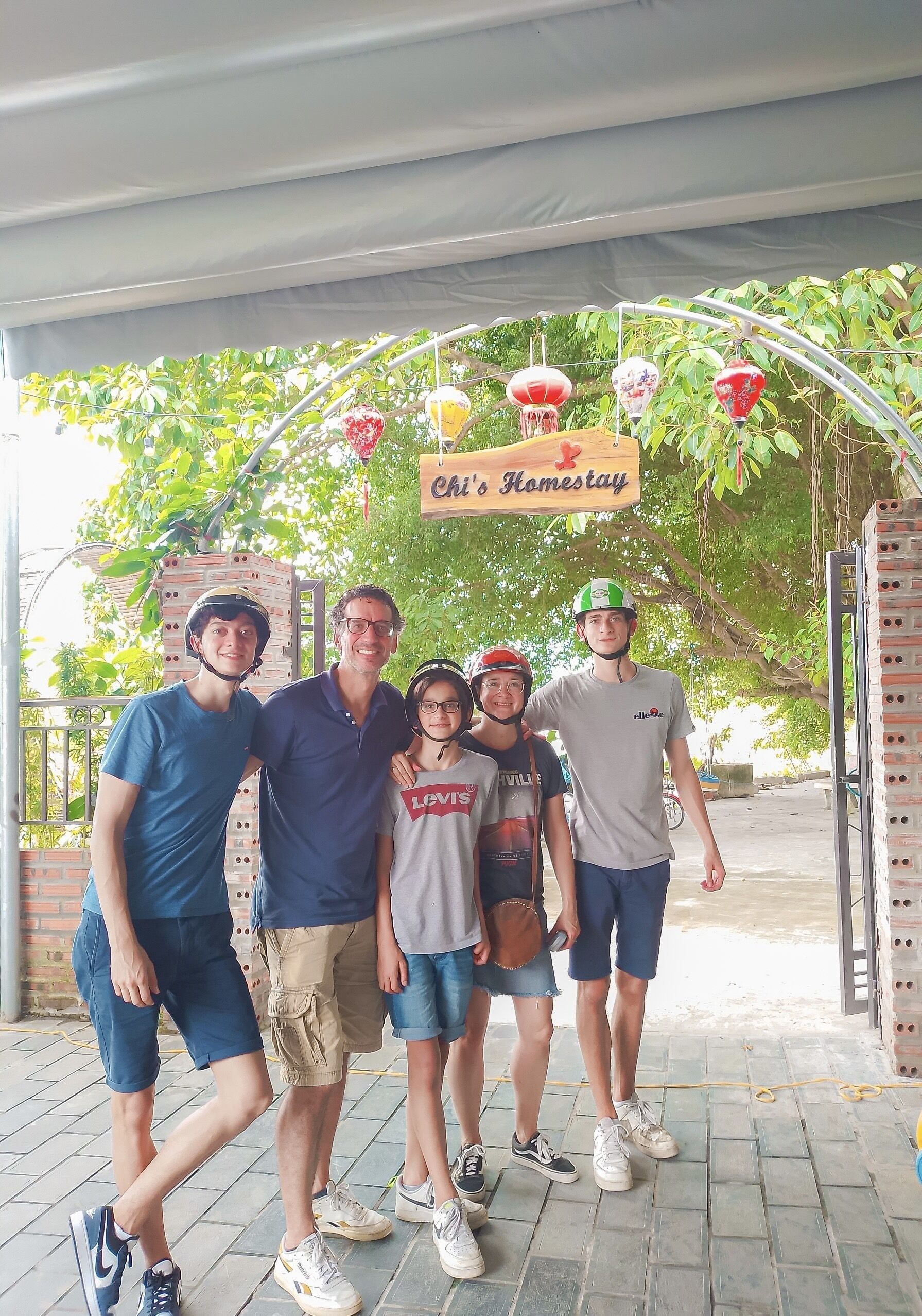 A group of people under a covered area with a sign reading "Chi's Homestay".