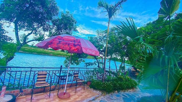 Un espace aménagé au bord de la rivière, avec un parasol, des chaises et un chemin en pierre, le tout aux couleurs de Coca-Cola.