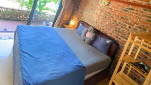 Une pièce avec un lit, un mur en briques, un plafond en bois et une fenêtre donnant sur un espace verdoyant.