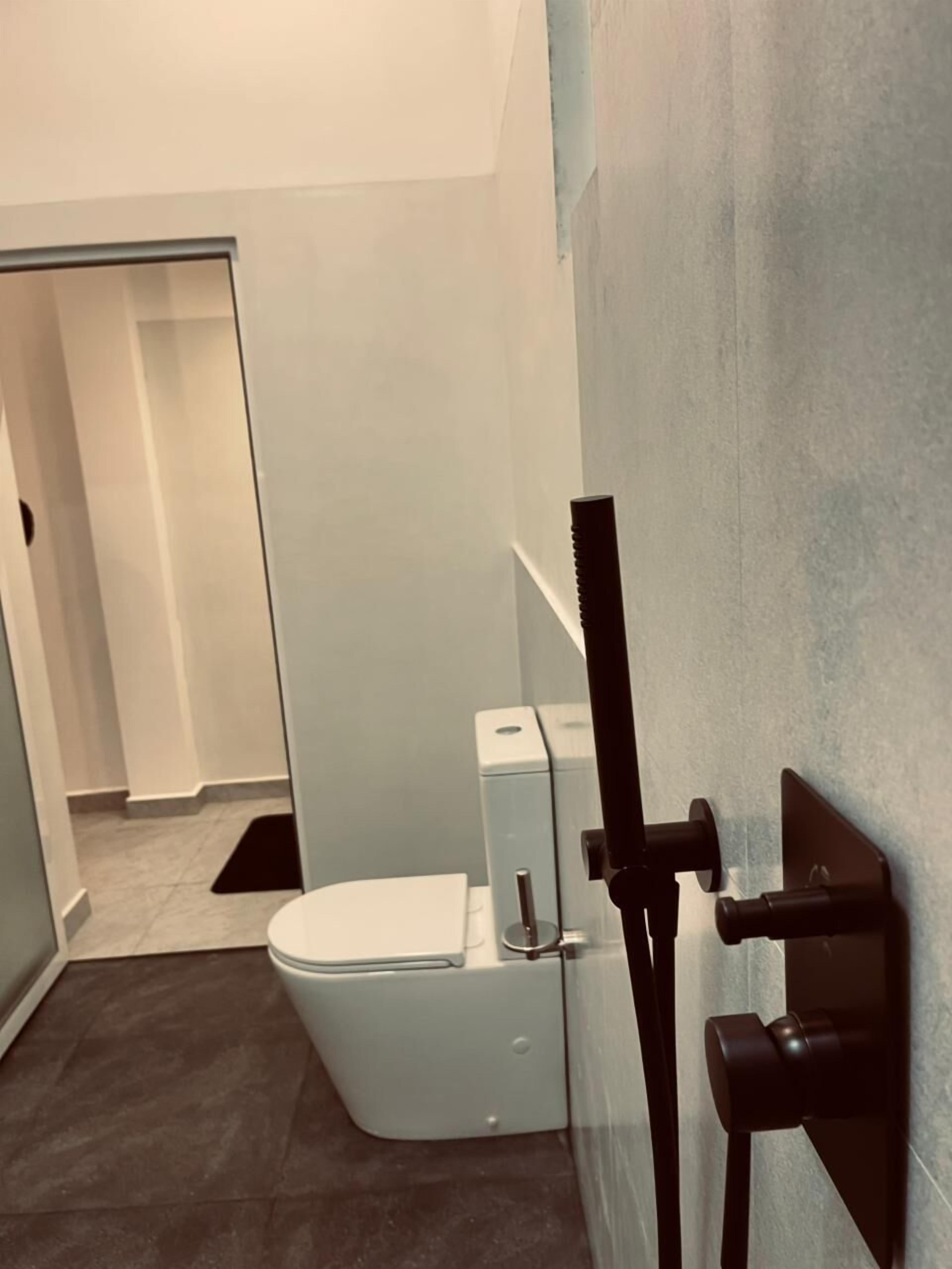 A modern bathroom with a toilet, a shower unit, and a visible door leading to another room.