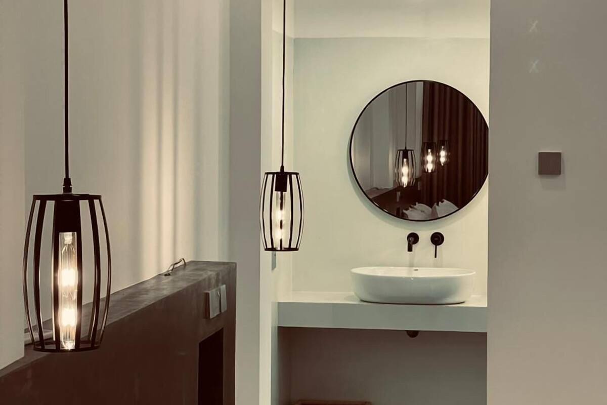 A modern bathroom with a large mirror, a round sink, and pendant lighting.