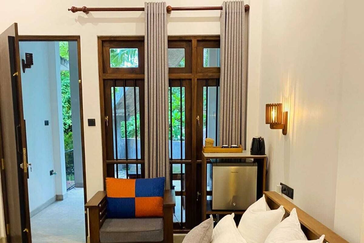 A hotel room with a bed, a desk, a chair, and a view of greenery outside.
