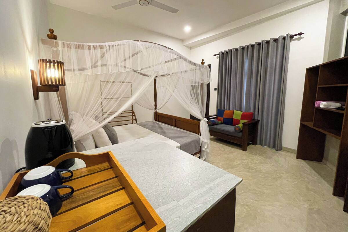 A bedroom with a bed, bedside table, chair, and a small table with cups.