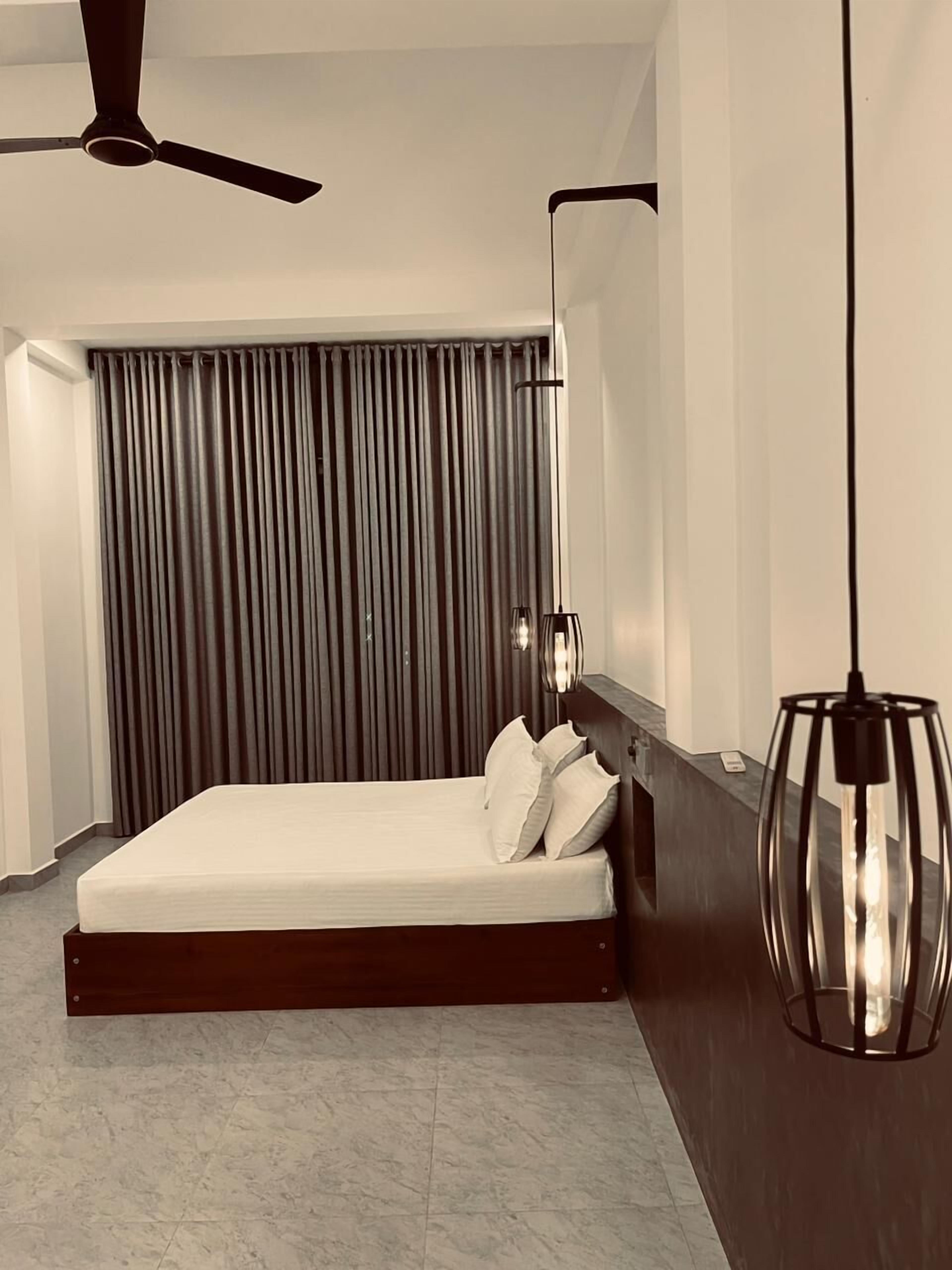 Une chambre moderne avec un lit, des rideaux, un ventilateur de plafond et un luminaire suspendu.