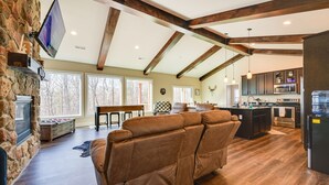 A spacious living area with a stone fireplace, a large brown leather sofa, and a kitchen with dark cabinets and stainless steel appliances. - 23-Acre Retreat | Wineries, Hiking & Fireplace (Roaring River)