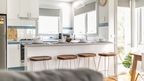 A modern kitchen with white cabinets, a central island with stools, a stove, and a microwave. - Ocean Breeze: 100m from the beach. Pet Friendly (Ocean Grove)