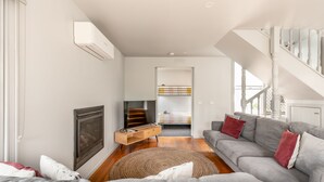 A modern living room with a sofa, a TV, a fireplace, and a staircase. - Ocean Breeze: 100m from the beach. Pet Friendly (Ocean Grove)