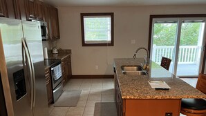 A kitchen with a stainless steel refrigerator, a built-in oven, a granite countertop, a sink, and a window with blinds. - Luxury Beach Side Home Ii 2 Bedroom Home by RedAwning (Norfolk)