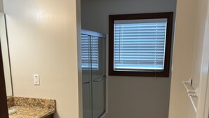 A small, well-lit bathroom with a shower, a window with blinds, a towel rack, and a trash bin. - Luxury Beach Side Home Ii 2 Bedroom Home by RedAwning (Norfolk)