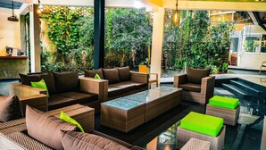 A modern lounge area with wicker furniture, a glass coffee table, and a view of lush greenery. - The Yacht Near CMB-Bandaranaike Intl. (Seeduwa - Katunayake)