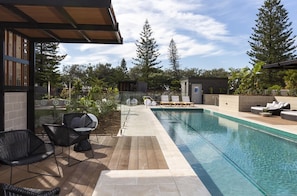 A swimming pool with lounge chairs, a wooden deck, and a view of trees.