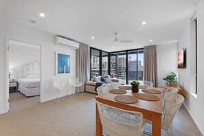 Un salon moderne avec un canapé, une table à manger et des chaises, de grandes fenêtres avec des rideaux et une vue sur la ville.