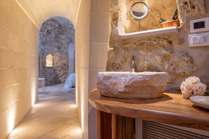 Ein Badezimmer mit Steinwänden, einem Holzbadezimmerfläschchen, einem Steintonne und einem Spiegel, dazu ein Rosenstrauß.