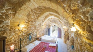 Ein Schlafzimmer mit Steinwänden, einem Bett, einem kleineren Bett und einem Nachttisch mit Lampe.