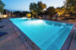 A rectangular swimming pool with a tiled edge, surrounded by a stone patio and a few lounge chairs. - Tenuta Bouganville With Garden And Pool (Carpignano Salentino)