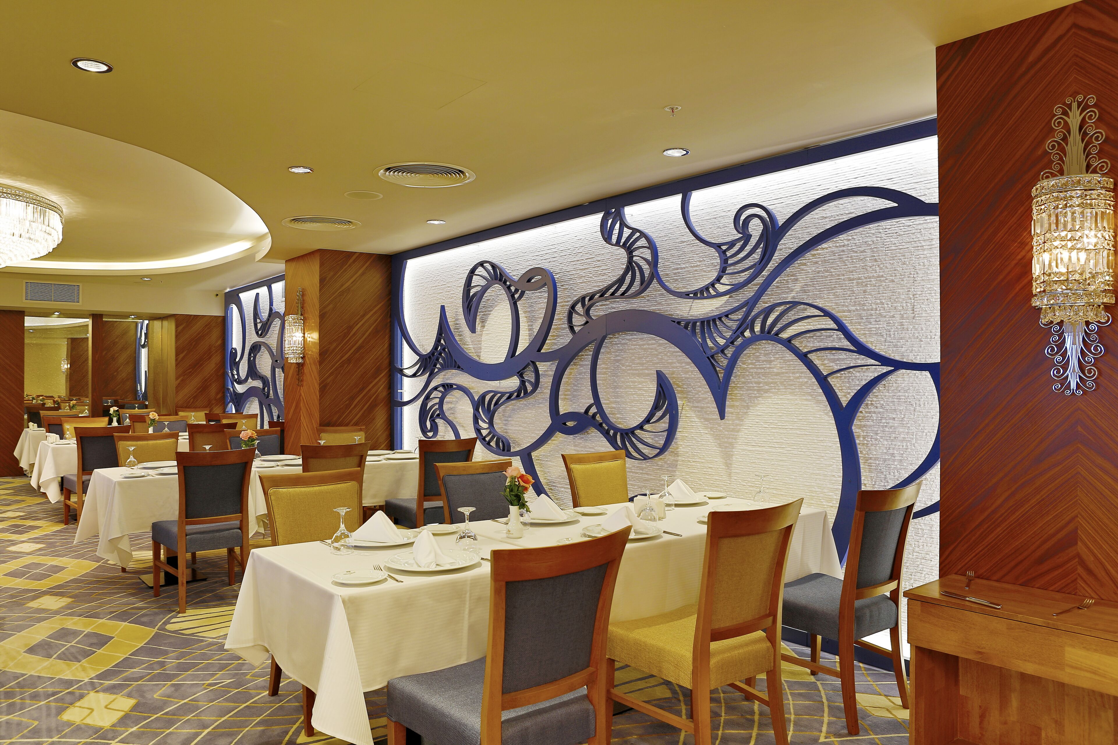 A dining area with tables set for service, chairs, and a decorative wall with abstract designs.