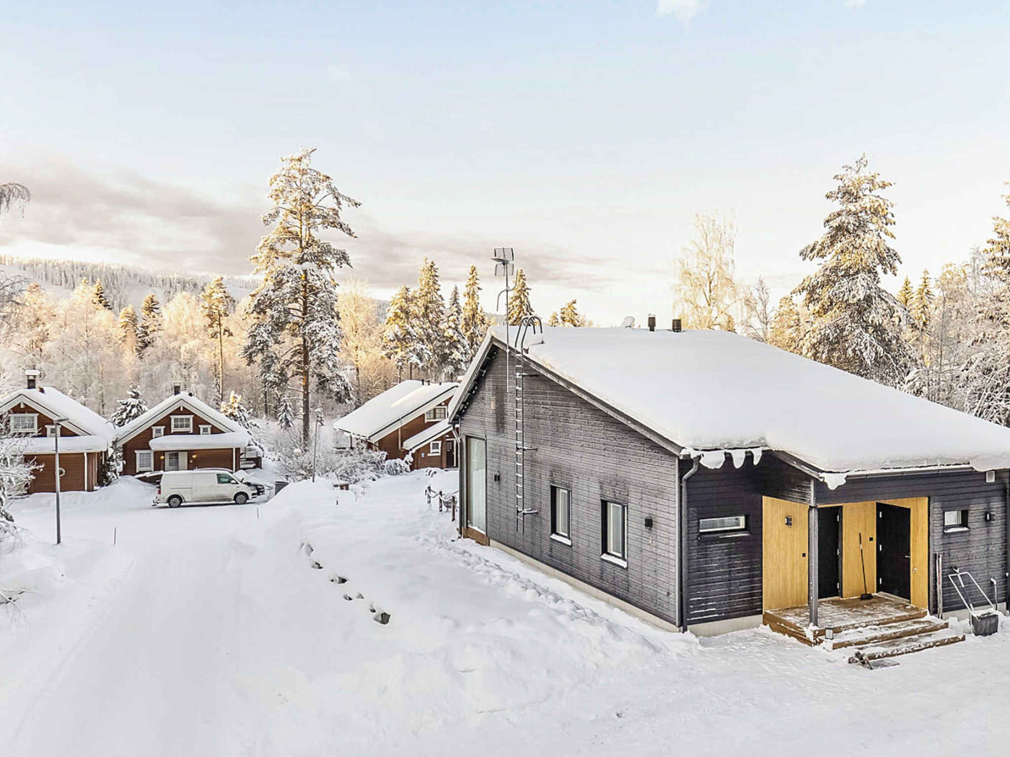 A snow-covered residential area with houses, a driveway, and a vehicle.