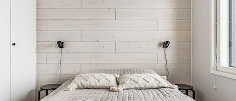 Un dormitorio con cama, dos mesitas de noche, una ventana y pared de madera.