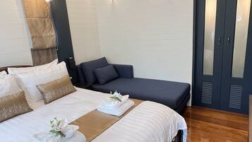 A hotel room with a large bed, a sofa, two wall-mounted lights, and a dark-colored wardrobe.