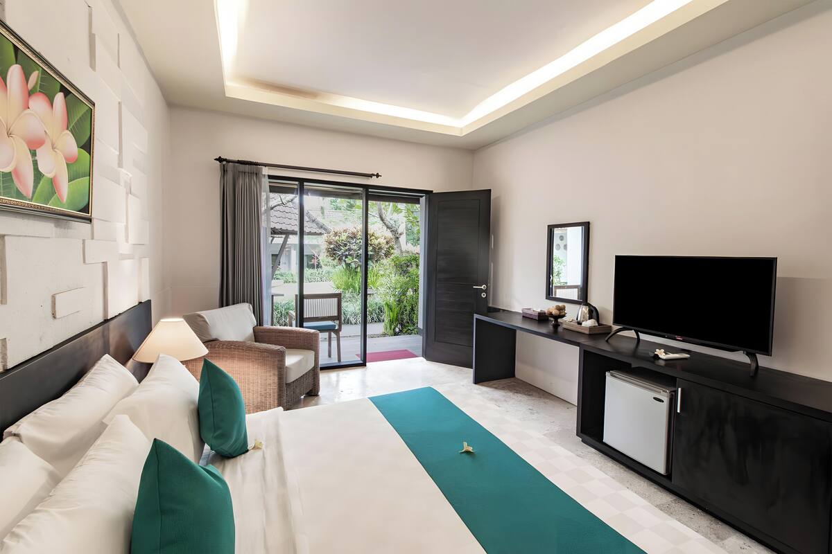 A hotel room with a bed, a desk, a television, and a sliding glass door leading to a balcony.