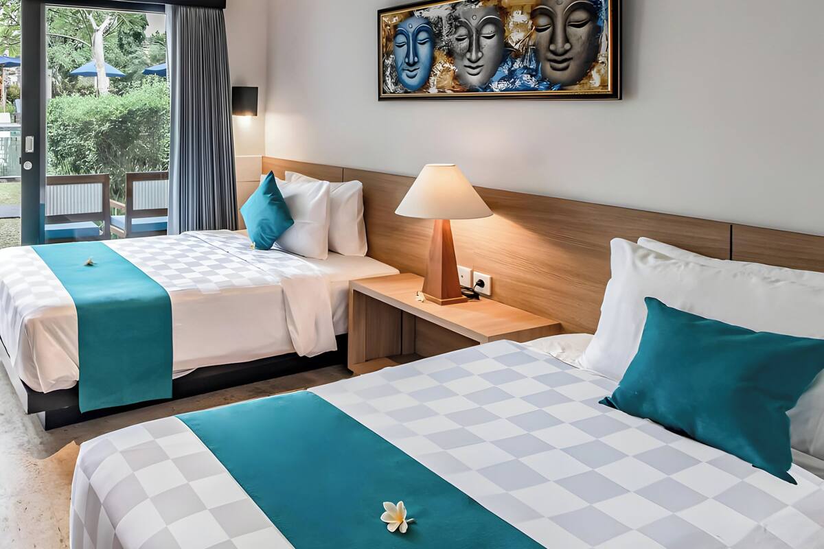 A hotel room with two beds, a wooden headboard, a nightstand with a lamp, and a painting on the wall.