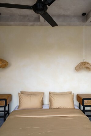 A bedroom with a bed, two pillows, a ceiling fan, and two woven wall hangings.