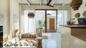 A modern living room with a sofa, a coffee table, and a TV. There are two hanging lights and a ceiling fan. - Liminal Palace Villa 2 by Betterplace (Canggu)