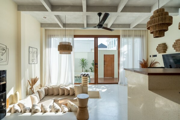 A modern living room with a sofa, a coffee table, and a TV. There are two hanging lights and a ceiling fan.