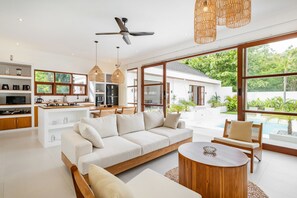 Een moderne woonkamer met een bank, salontafel en een eethoek. Een groot raam biedt uitzicht op groen en een zwembad.