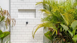 Un mur en briques blanches avec une douche intégrée, une petite étagère et une porte.