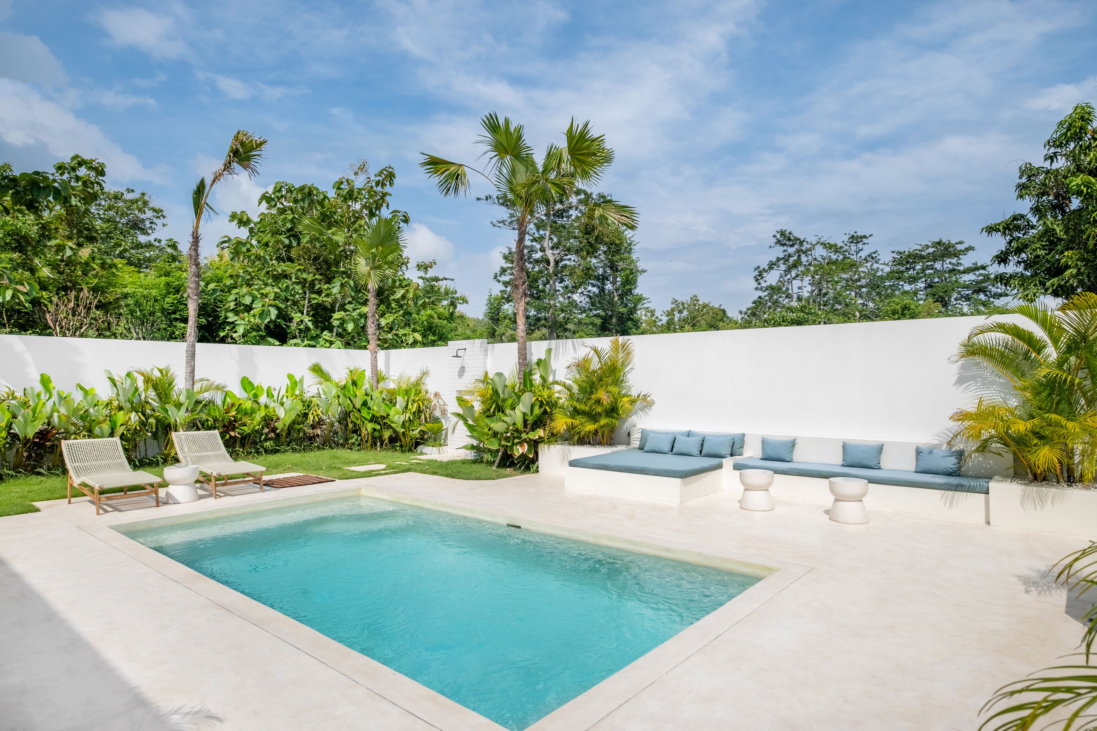 A swimming pool with lounge chairs and a seating area, surrounded by lush greenery and palm trees.
