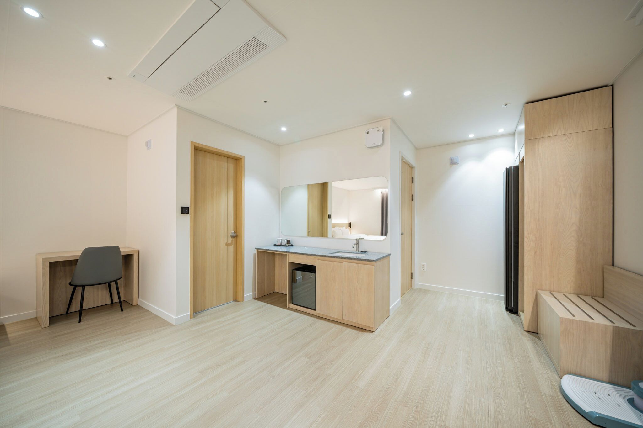 Una habitación moderna y minimalista con un escritorio de madera, un lavabo integrado y un espejo grande.
