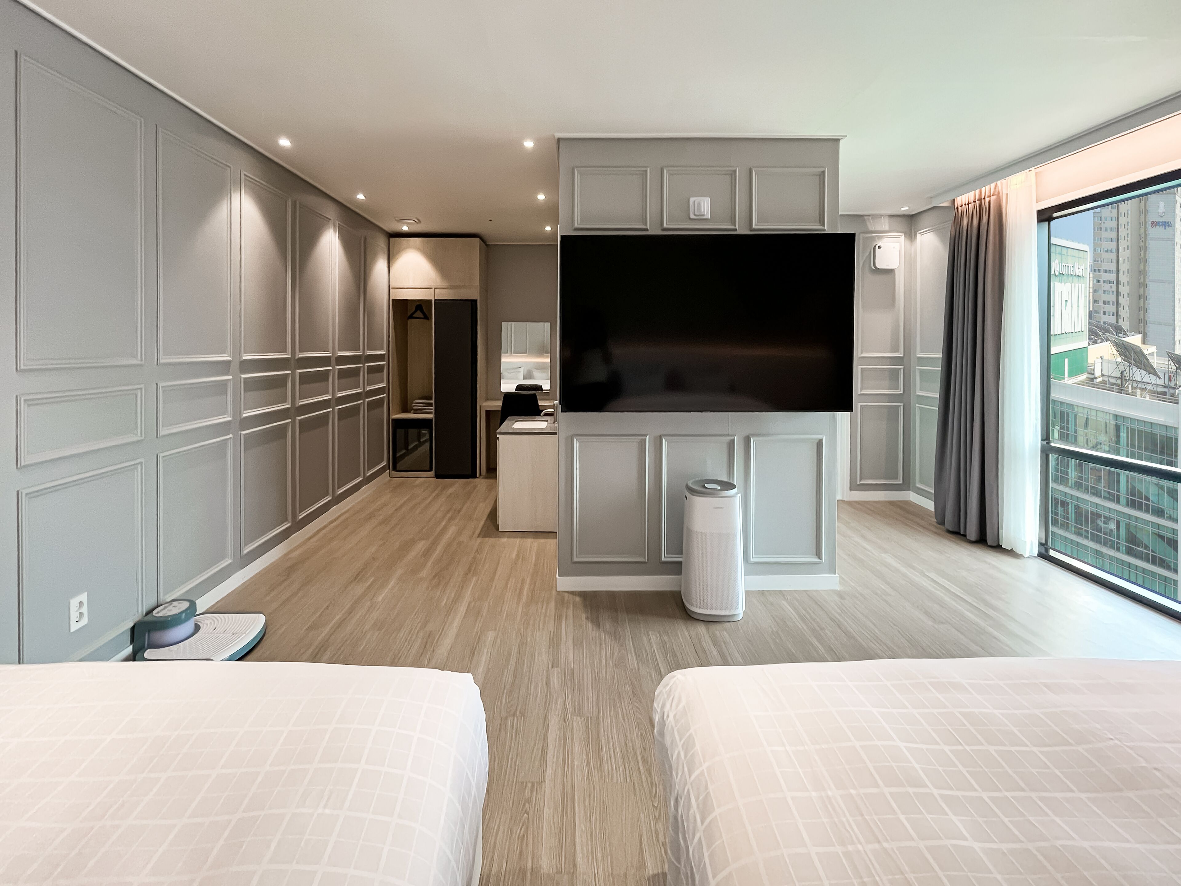 A hotel room with a large TV, a desk, and a balcony with a city view.
