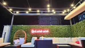 Een terras met rieten meubels en een neonbord.