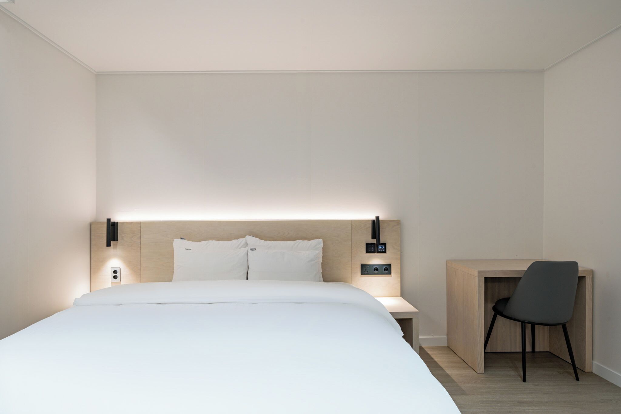 A modern hotel room with a large bed, bedside tables, a desk, and a chair.