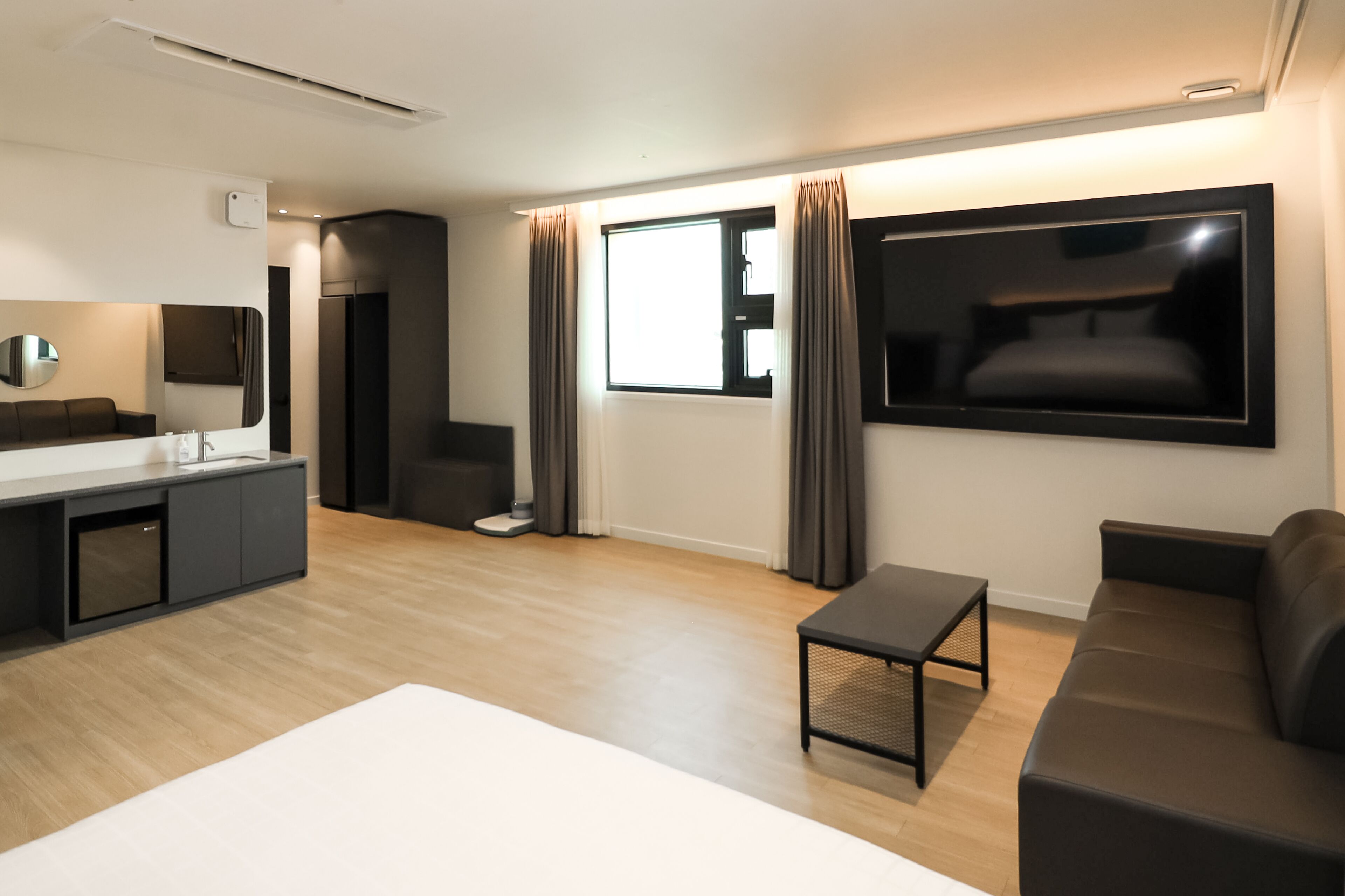 A modern living room with a sofa, a coffee table, a TV, and a kitchen area with a counter and cabinets.