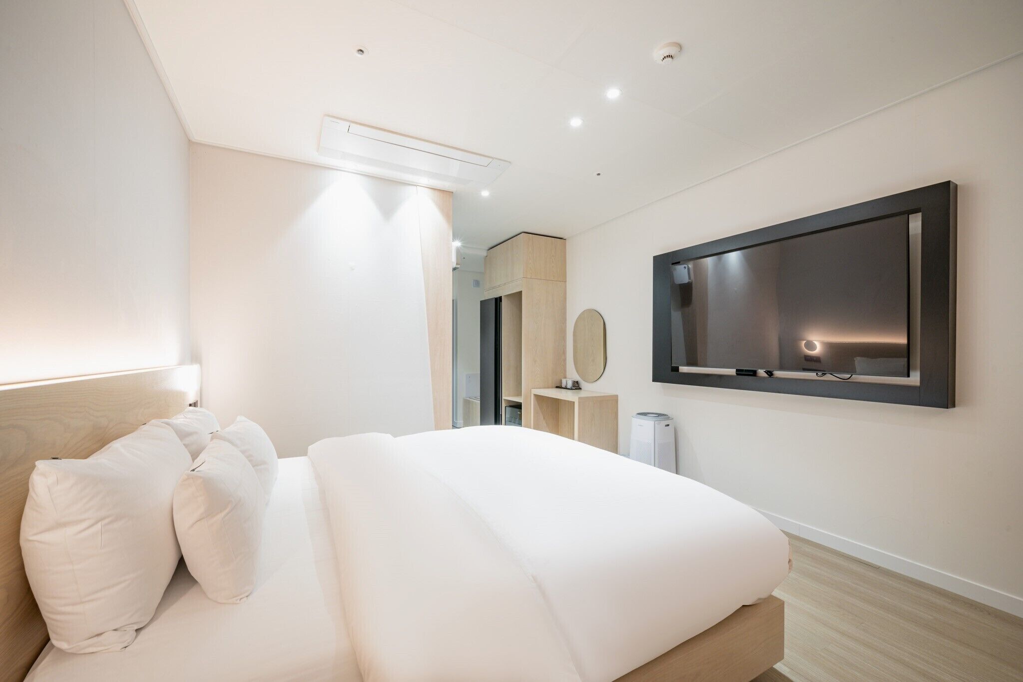 A modern hotel room with a large bed, a flat-screen TV mounted on the wall, and a minimalist design.