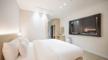 A modern hotel room with a large bed, a flat-screen TV mounted on the wall, and a minimalist design.