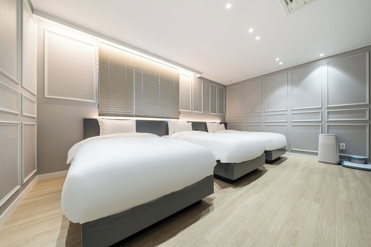 Een moderne slaapkamer met twee bedden, een groot raam met zonwering en een ingebouwde luchtreiniger.