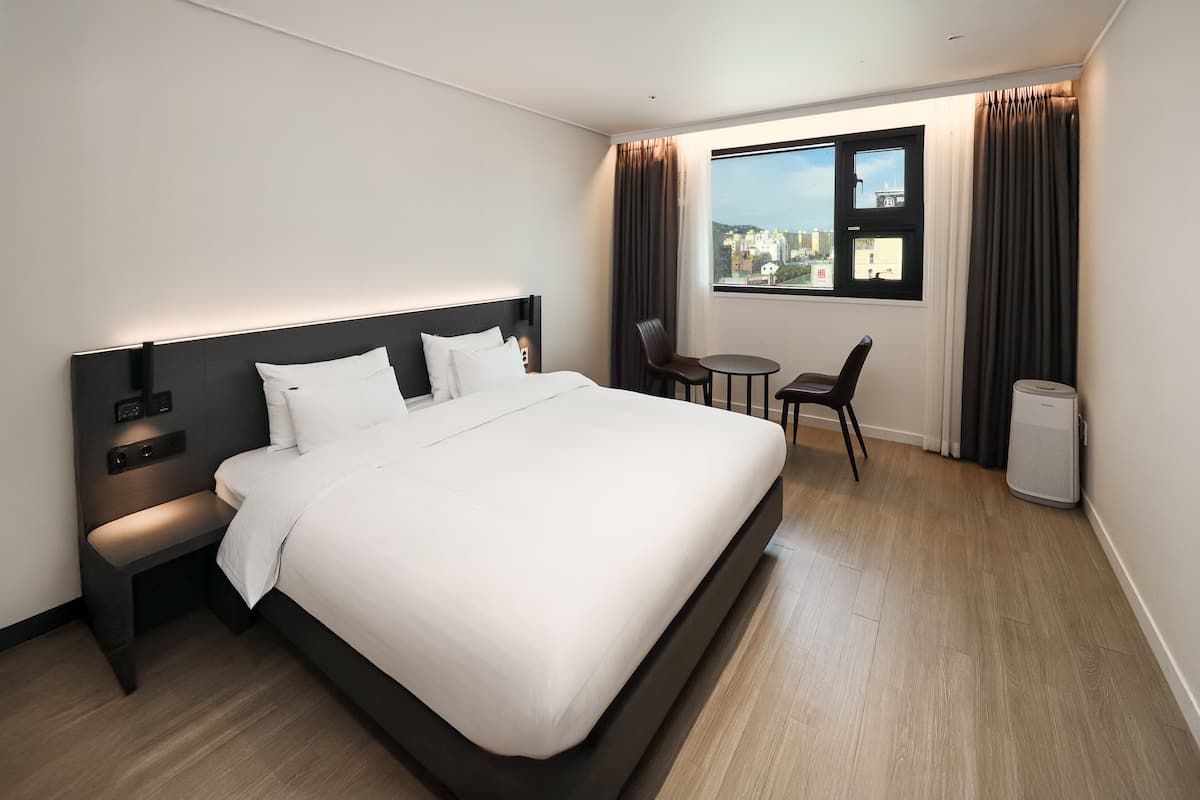 Een moderne hotelkamer met een groot bed, nachtkastje en een klein bureau met stoel.