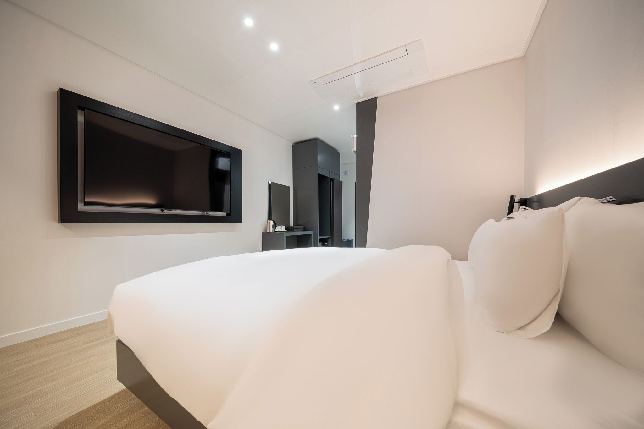 A modern hotel room with a large bed, a flat-screen TV mounted on the wall, and a built-in wardrobe.