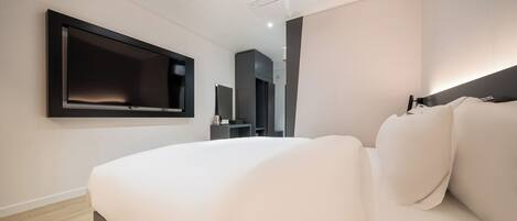 A modern hotel room with a large bed, a flat-screen TV mounted on the wall, and a built-in wardrobe.