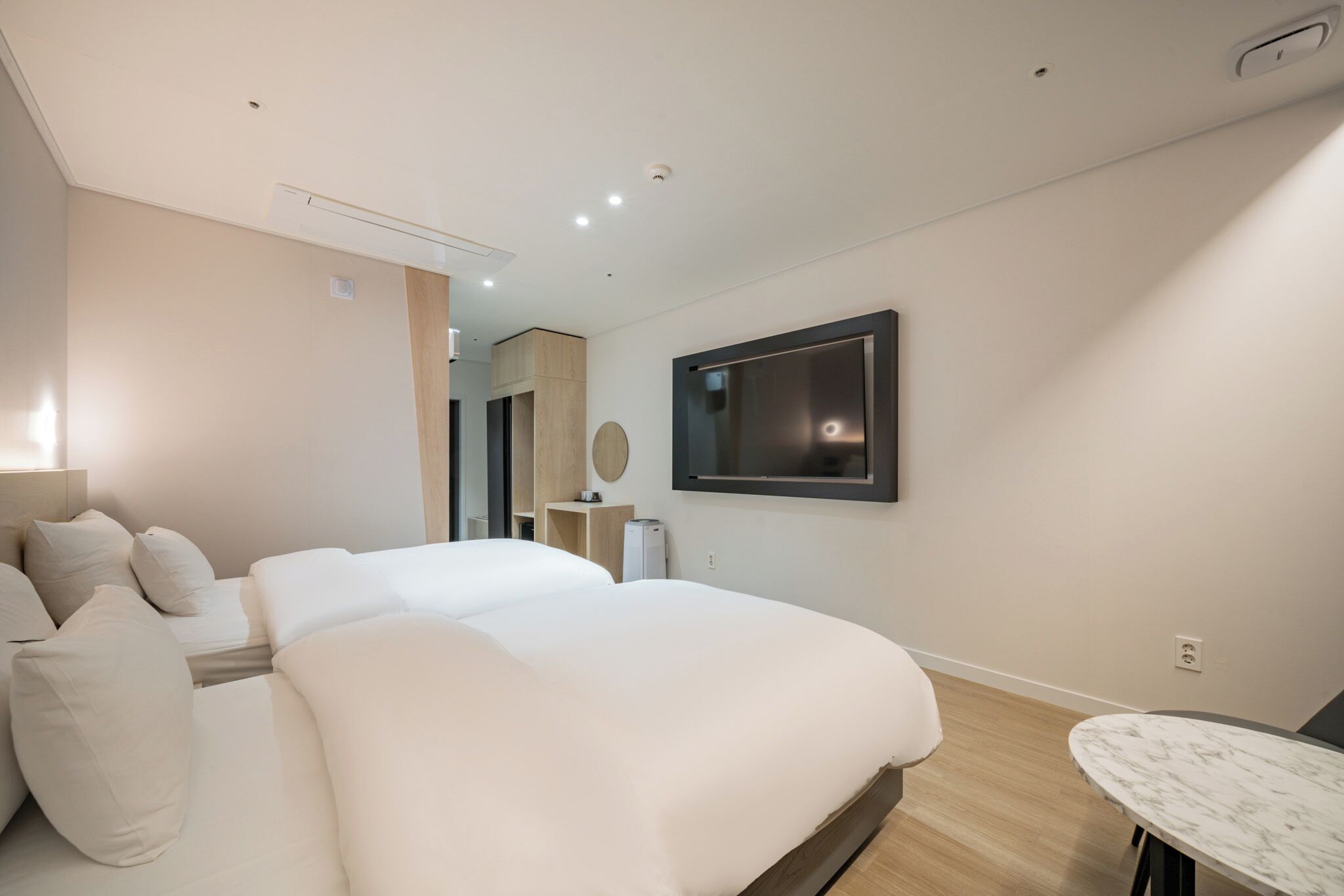 A modern hotel room with a large bed, a flat-screen TV mounted on the wall, and a small table.