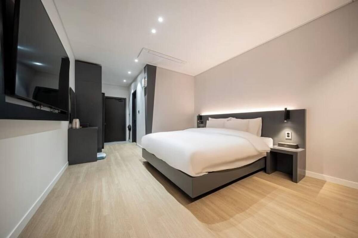 Een moderne slaapkamer met een bed, nachtkastje en een aan de muur bevestigde televisie.