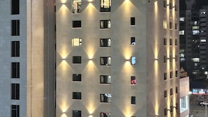 Een modern gebouw met het bord "HOUND HOTEL" bovenop. Het heeft meerdere verdiepingen met gelijkmatig verdeelde ramen en een plat dak.