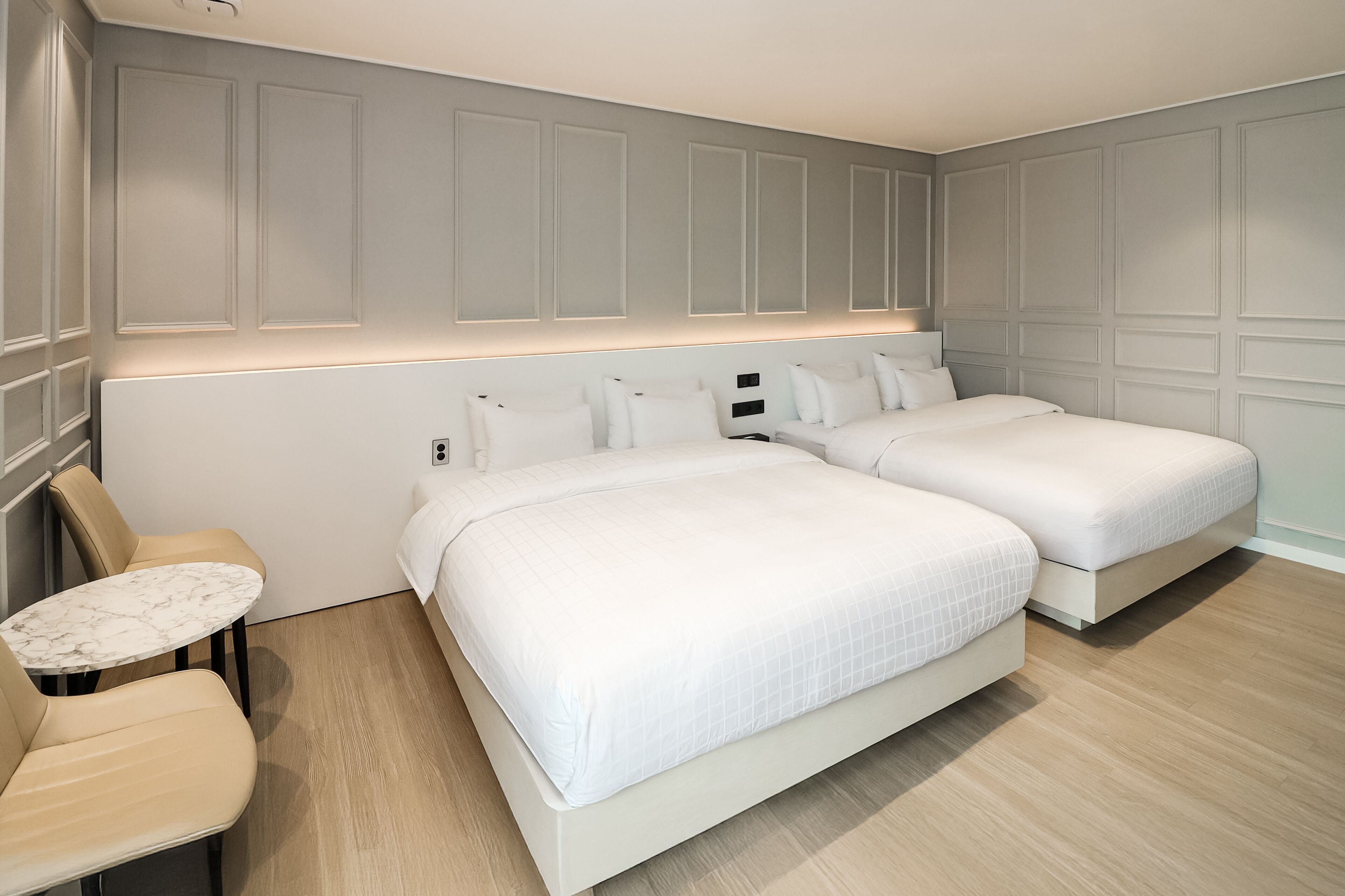 A hotel room with two beds, a small round table, and a chair.