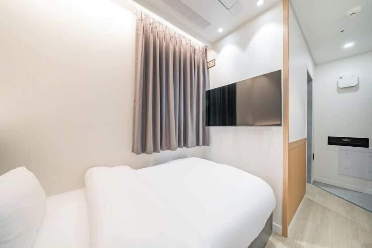 Een hotelkamer met een bed, gordijnen, een flatscreen-tv en een kleine badkamer.