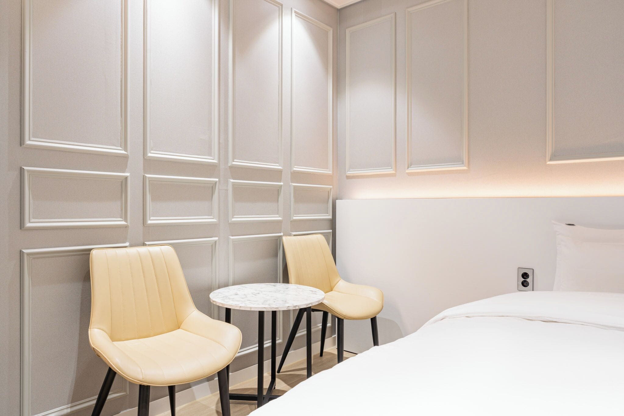 Een hotelkamer met een bed, twee stoelen, een klein rond tafeltje en een wandlamp.